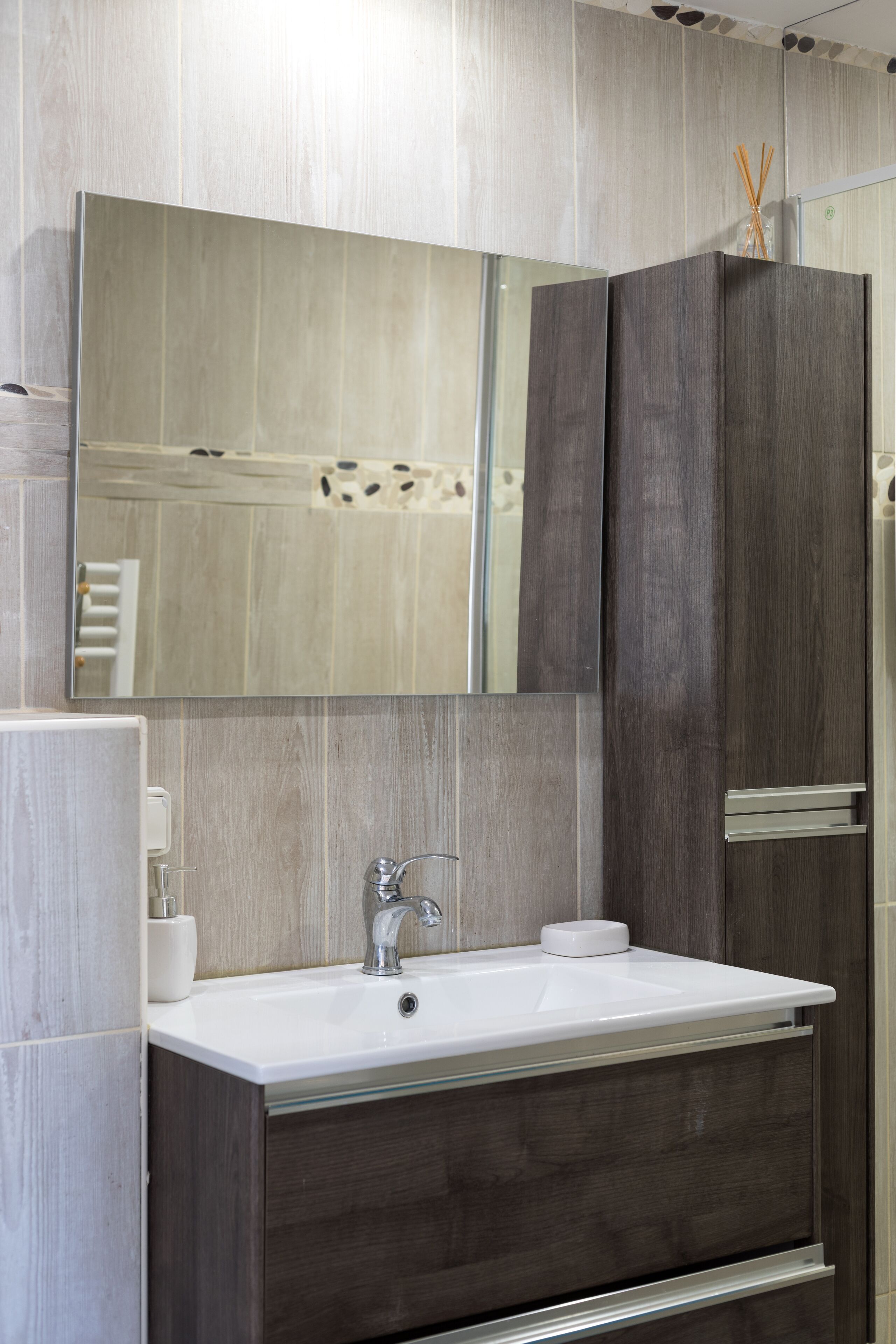 A modern bathroom with a large mirror, a white sink, and dark wood cabinetry.
