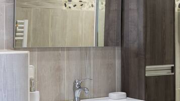 A modern bathroom with a large mirror, a white sink, and dark wood cabinetry.