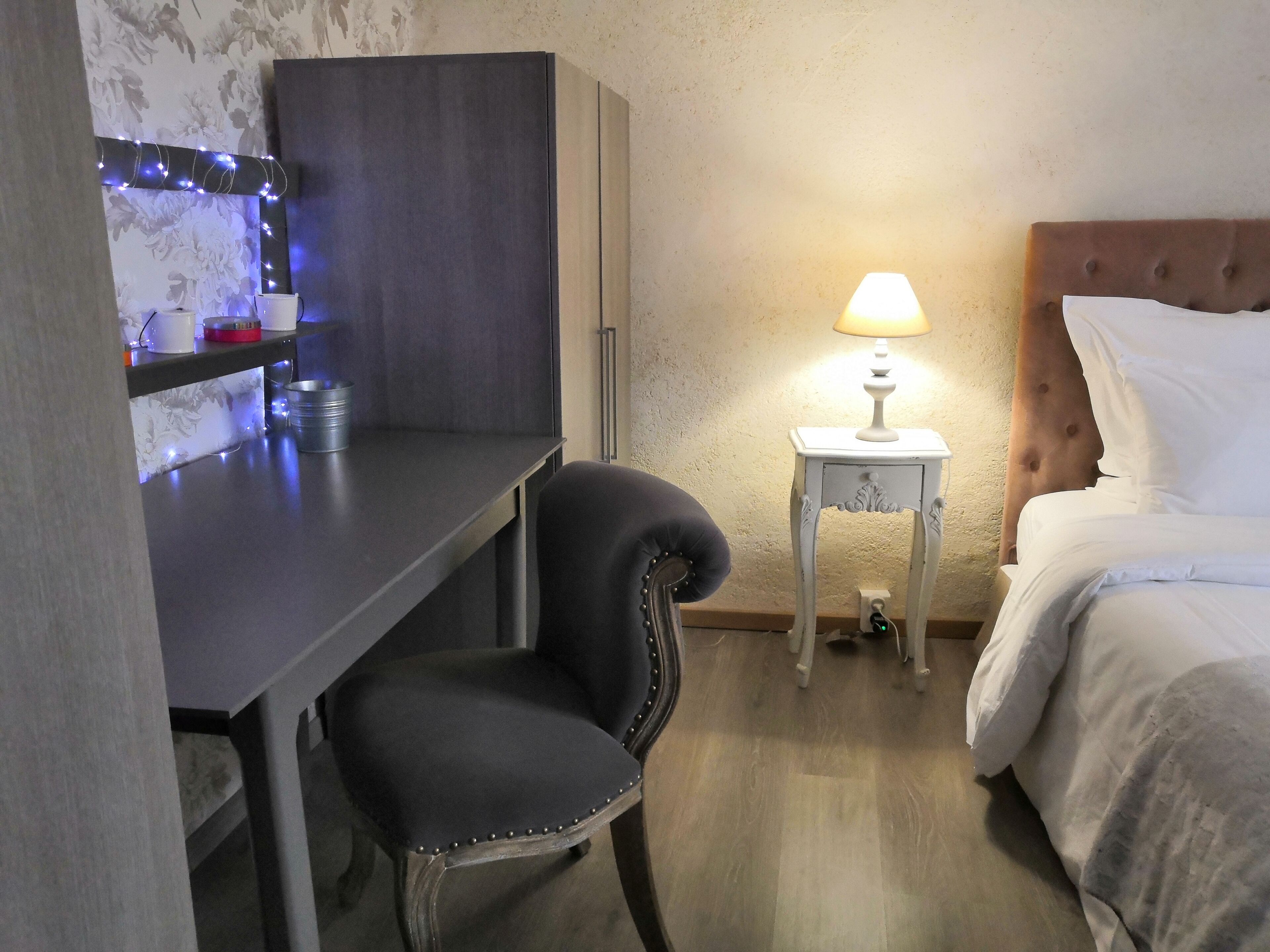Une chambre d’hôtel comprenant un lit, une table de chevet avec une lampe, un bureau avec une chaise et une étagère fixée au mur, agrémentée de lumières décoratives.