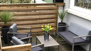 Un terrazzo in legno con un divano grigio, due poltrone e un tavolino con un vaso di fiori gialli.