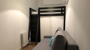 Una stanza con una cuccetta, un divano grigio, un cuscino blu e un termosifone.