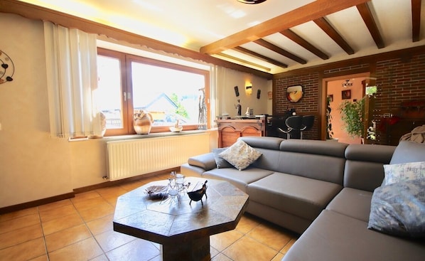 A cozy living room with a large sofa, a coffee table, and a window with curtains.
