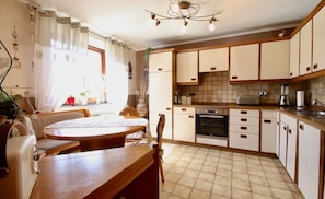A kitchen with a dining area, featuring a wooden table and chairs, a built-in oven, and cabinets.
