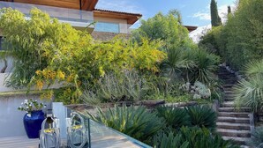 Une maison moderne dotée d’une terrasse en bois, d’une petite piscine et d’une grande variété de plantes et d’arbres.