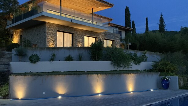 Une maison moderne avec une façade en pierre, de grandes fenêtres et une piscine en premier plan.
