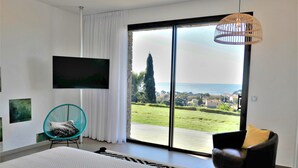Une chambre dotée d’un grand lit, d’un téléviseur fixé au mur, d’un fauteuil et offrant une vue sur la mer grâce à une porte-fenêtre coulissante.