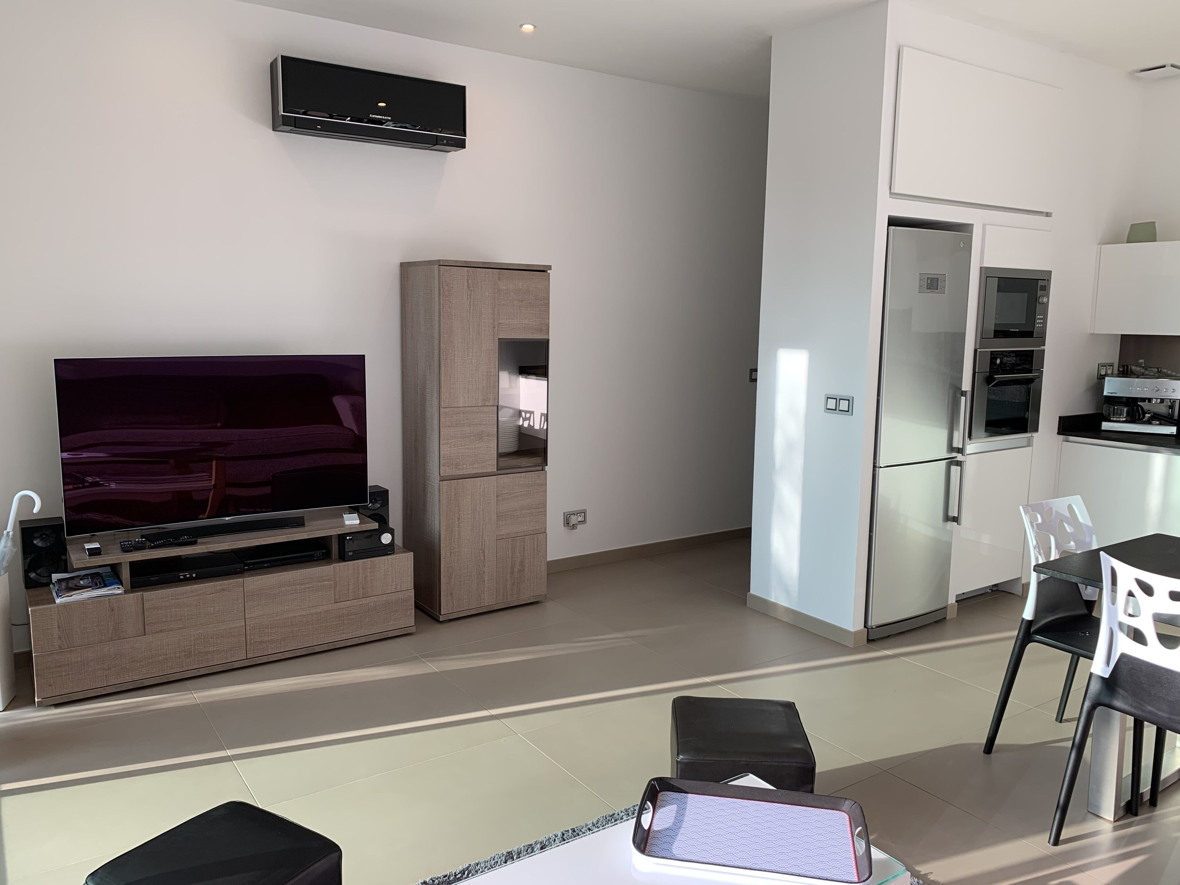 Una sala moderna con televisor de pantalla plana, un mueble de madera y una zona de comedor con una mesa y sillas.