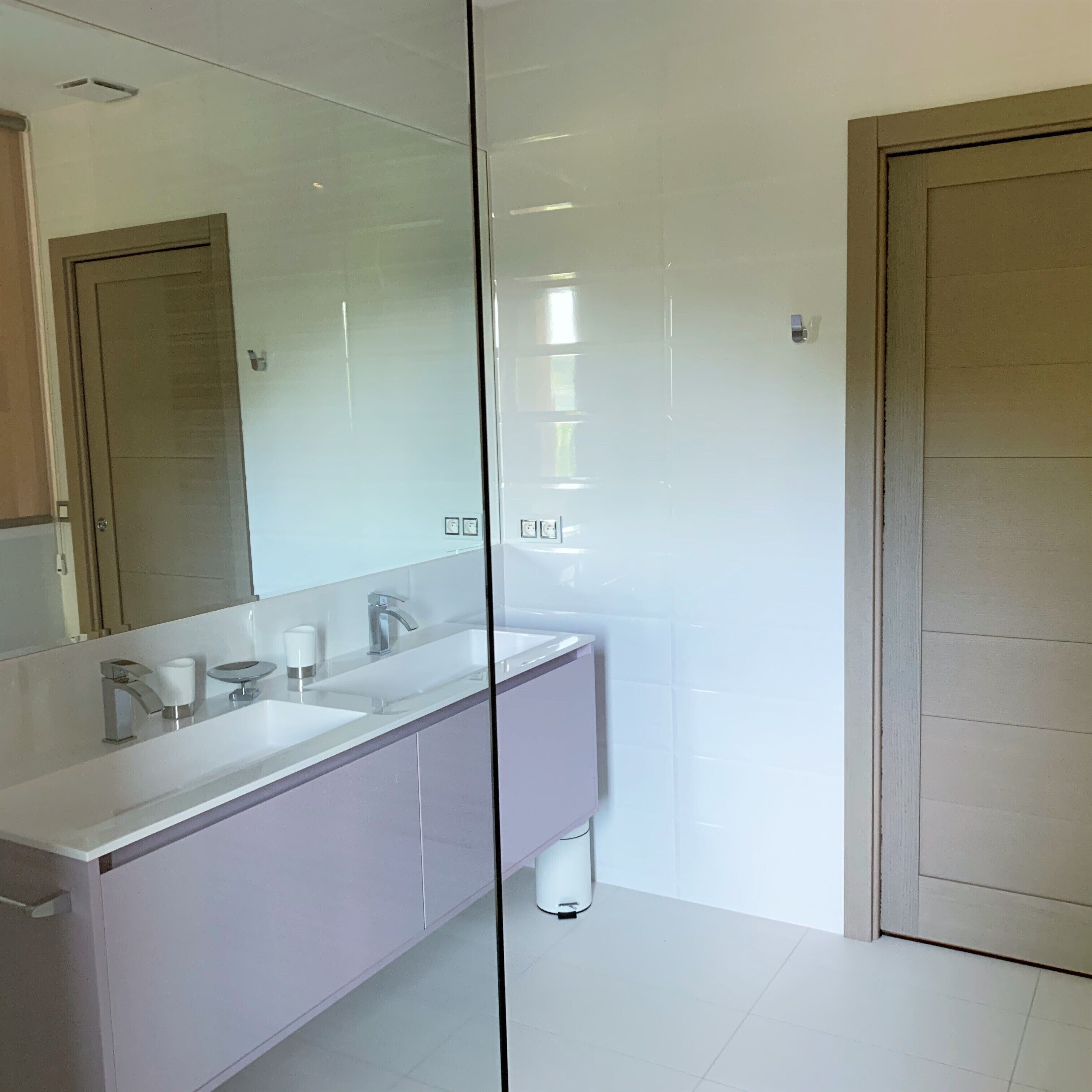 A modern bathroom with two sinks, a large mirror, and a glass partition.