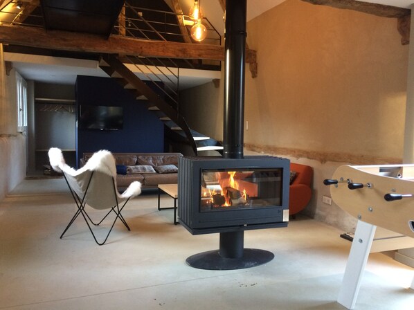 A cozy living room with a wood-burning stove, a sofa, a chair, and a foosball table. - Les Prés de la Rivière, Maintenay (Maintenay)
