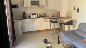 Una sala de estar moderna con un sofá gris, una mesa de centro de madera y una cocina con armarios blancos y un microondas.