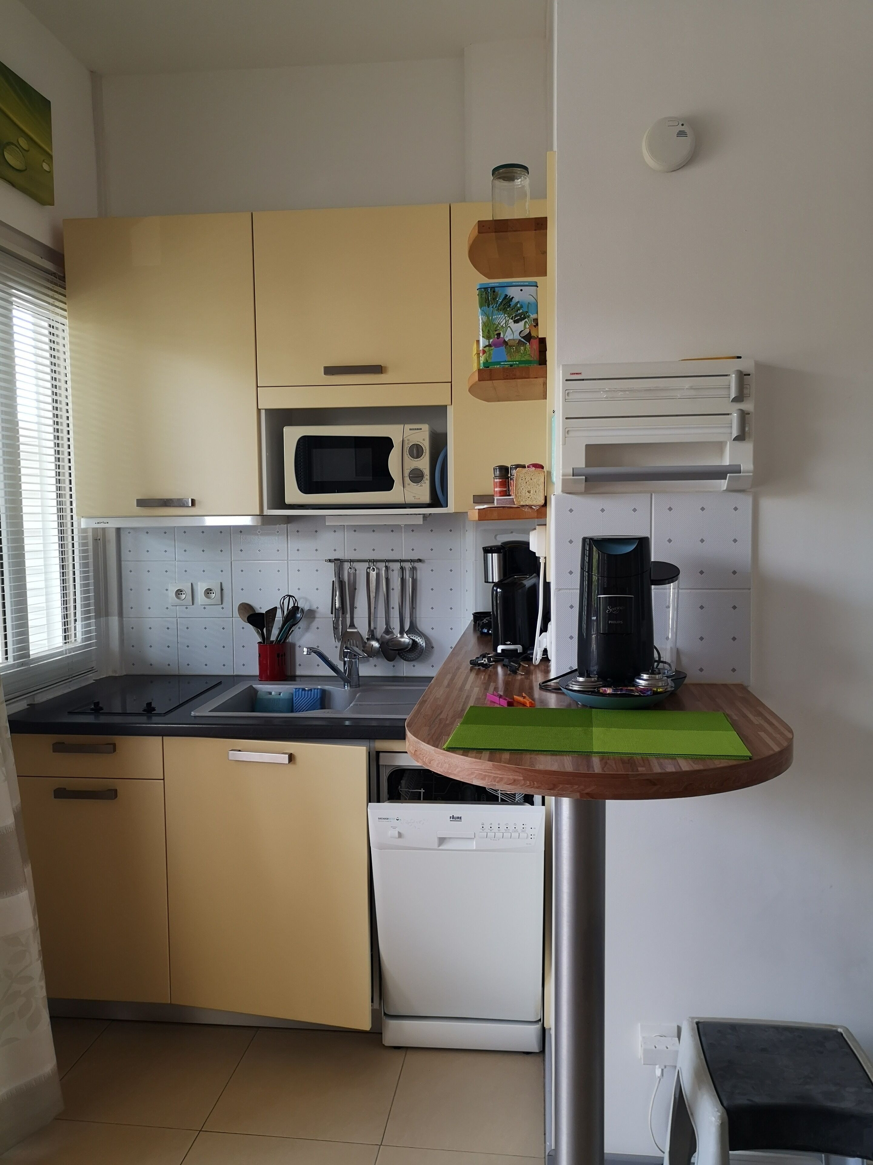 Une cuisine de taille réduite avec des meubles de couleur beige, un four à micro-ondes, une machine à café et un lave-vaisselle.