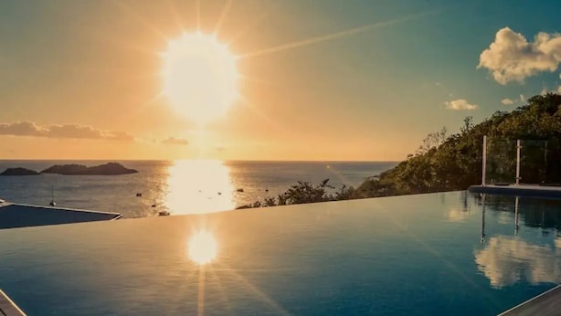 Une piscine à débordement offrant une vue sur le coucher de soleil, une terrasse en bois et un ciel dégagé.