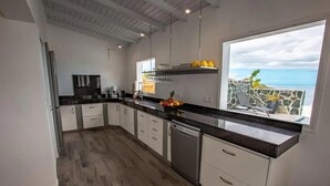Une cuisine moderne avec des armoires blanches, un comptoir noir et une vue sur l’océan grâce à une grande fenêtre.