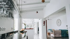 Une cuisine spacieuse équipée d’appareils électroménagers modernes, un coin repas avec une table à plateau en verre, et un salon avec un canapé et une horloge au mur.