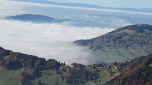 A panoramic view of a mountainous landscape with a village nestled among rolling hills and autumn-colored trees.