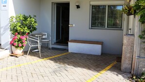 A paved entrance with a bench, a potted plant, and a door leading inside.