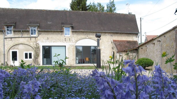 A rustic building with a large arched doorway, a glass door, and a small window.