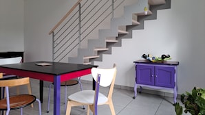 A modern kitchen with a staircase, a dining table with chairs, a purple cabinet, and a potted plant.