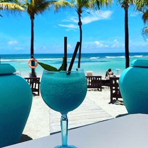 A tropical drink on a table with a view of the ocean and palm trees.
