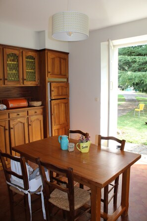 A wooden dining table with chairs, a pitcher, and a mug. There is a window with a view of a garden. - Villa 6-10 pers in Espalion in Aveyron, at the gateway to Aubrac (Espalion)