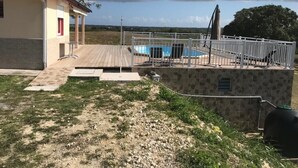 A pool area with a wooden deck, a stone wall, and a covered seating area.