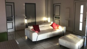 A modern living room with a white sofa, a matching ottoman, and two doors.