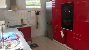 A kitchen with red cabinets, a stainless steel refrigerator, and a window with blinds.