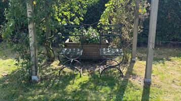 Een houten pergola met lichtjes, een metalen tafel en stoelen eronder, omringd door weelderige begroeiing.