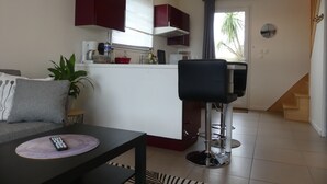 A compact living space with a kitchenette, a dining area, and a staircase. - COTTAGE IDEALLY LOCATED (Saint-Évarzec)