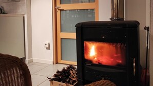 Una sala de estar con estufa de leña, muebles de mimbre y una puerta con paneles de vidrio.