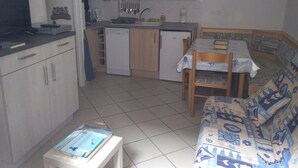 Una cocina compacta con microondas, lavamanos y un refrigerador pequeño. Hay un comedor con mesa y sillas, además de un sofá.