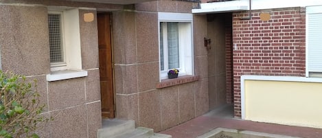 A two-story building with a stone facade, a wooden door, and a small window with a flower pot.