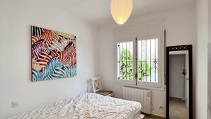 Ett sovrum med en säng, en stol, ett fönster med galler, ett element och en dörr.