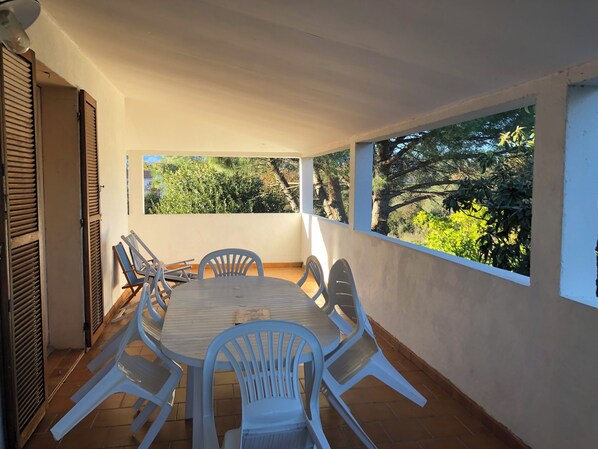 A covered patio with a round table and chairs, large windows, and a view of greenery. - Mare è Monte 4,5 km from the sea. Ideal for touring Corsica (Ghisonaccia)