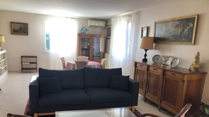 A living room with a dark blue sofa, a glass coffee table, and a patterned armchair. There is a wooden cabinet with decorative items and a painting on the wall. - Mare è Monte 4,5 km from the sea. Ideal for touring Corsica (Ghisonaccia)