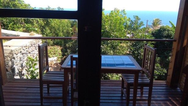 Une terrasse en bois avec une table et des chaises, offrant une vue sur un paysage rocheux et l’océan.