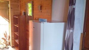 Une pièce de taille modeste, avec un intérieur en bois, un réfrigérateur blanc, une armoire en bois et un lit recouvert d’une courtepointe à rayures.