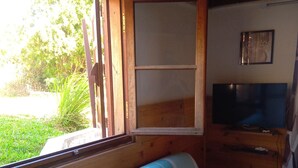 Une pièce avec un banc en bois, un téléviseur posé sur un meuble en bois et une fenêtre donnant sur un paysage verdoyant.