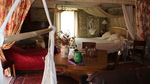 Una habitación con una cama, una mesa de madera con un florero, una silla y un sillón colgante.
