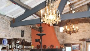 Un comedor rústico con mesa y sillas de madera, una araña y una pared de piedra con chimenea.
