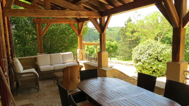 Eine Terrasse im Freien mit einem Holztisch und -stühlen, einer Couch mit Kissen sowie Korbstühlen.