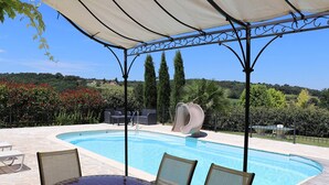 Ein Pool mit Rutsche, umgeben von einer überdachten Terrasse mit Stühlen und einem Tisch.