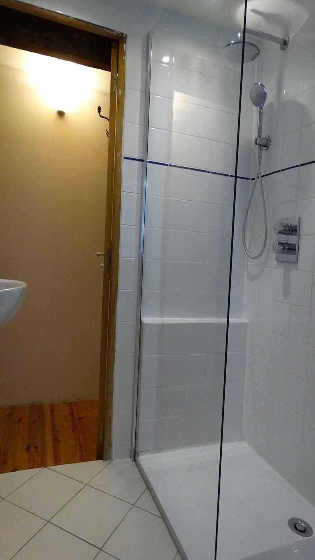 Ein Badezimmer mit Duschkabine aus Glas, einem Waschbecken und einer Holztür.