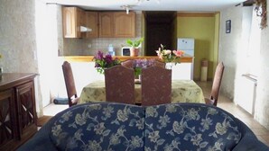A living room with a sofa, a dining table with chairs, and a kitchen in the background.
