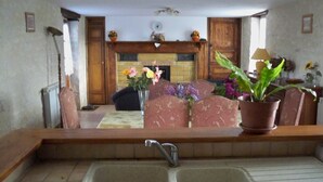 A kitchen with a double sink, a dining area with patterned chairs, and a fireplace with decorative items.