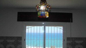A room with a view of the ocean through a barred glass door, a decorative hanging light fixture, and patterned wall tiles. - PANORAMIC HOUSE DAR TINDA (Asilah)