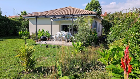 A house with a tiled roof, a covered patio with chairs, and a lawn.