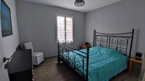 A bedroom with a bed, a chair, a desk, a window, and a ceiling light fixture.