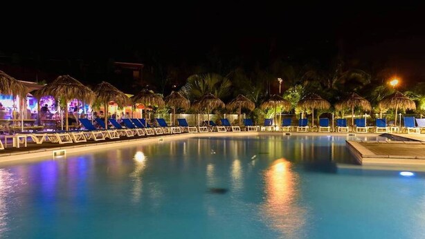 A nighttime swimming pool with lounge chairs and thatched umbrellas, surrounded by palm trees. - Farniente in Martinique (Le Vauclin)
