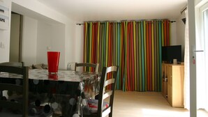 Un coin repas avec une table, des chaises et une tasse rouge. Un rideau à rayures colorées se trouve à l’arrière-plan.